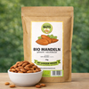 Bio Mandeln naturbelassen von Awesome Nuts im Beutel neben einer Schale mit Mandeln auf Holztisch vor grünem Naturhintergrund